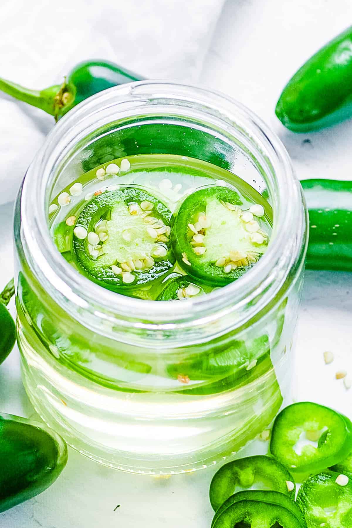 Jalapeno simple syrup in a gl، mason jar, garnished with jalapeno slices.