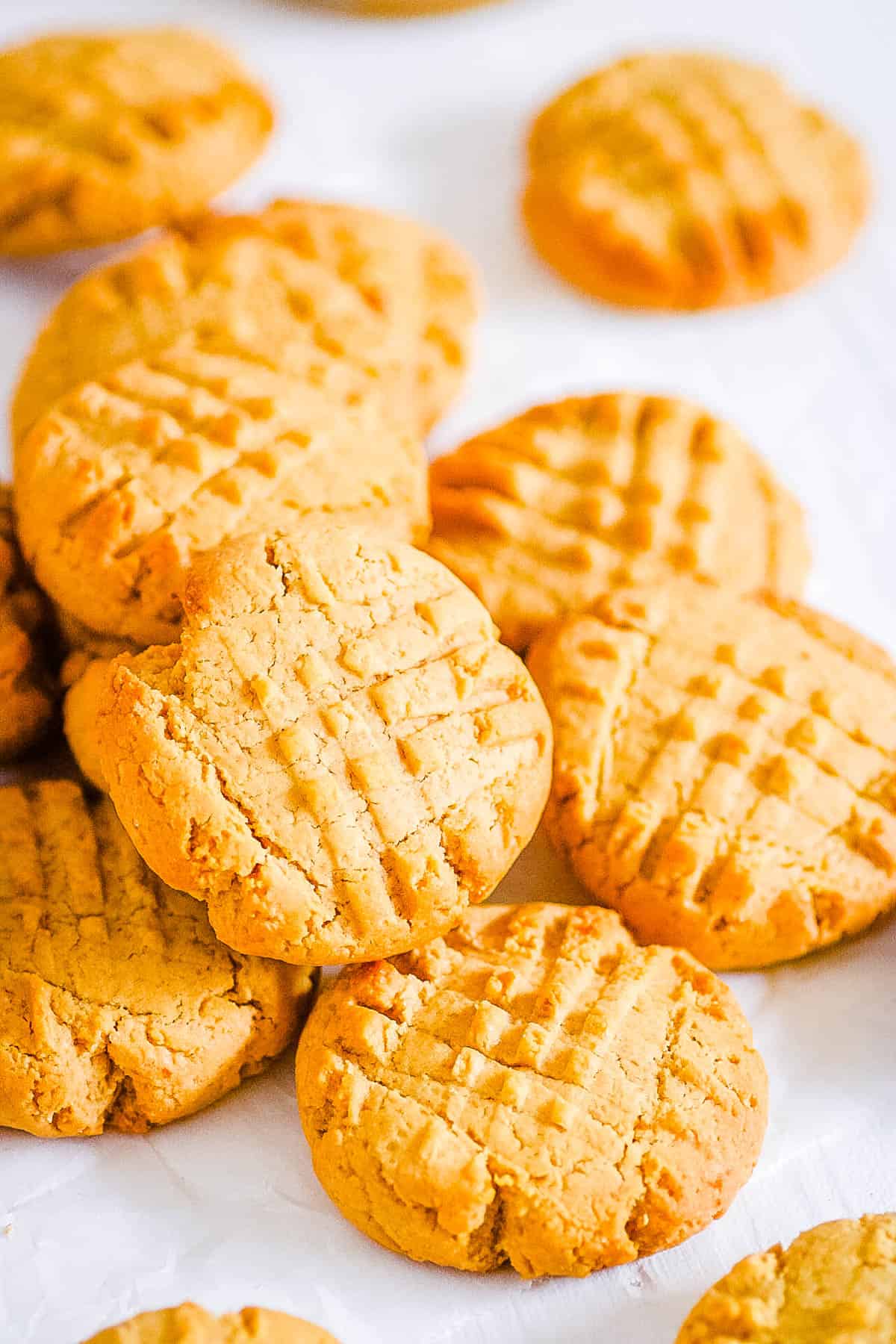 Peanut butter powder cookies stacked on a sheet of parchment paper.