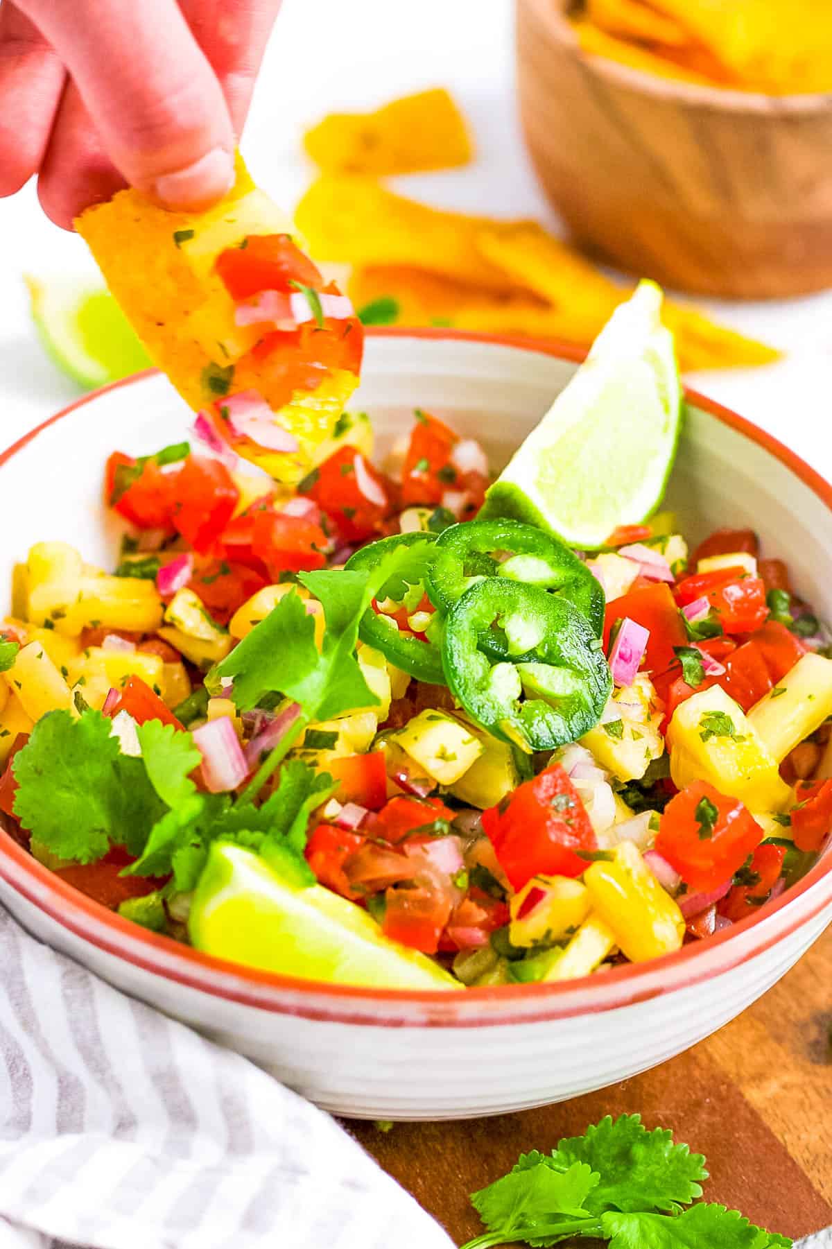 Pineapple pico de gallo served in a white bowl, topped with jalapenos, with a chip being dipped into the bowl.