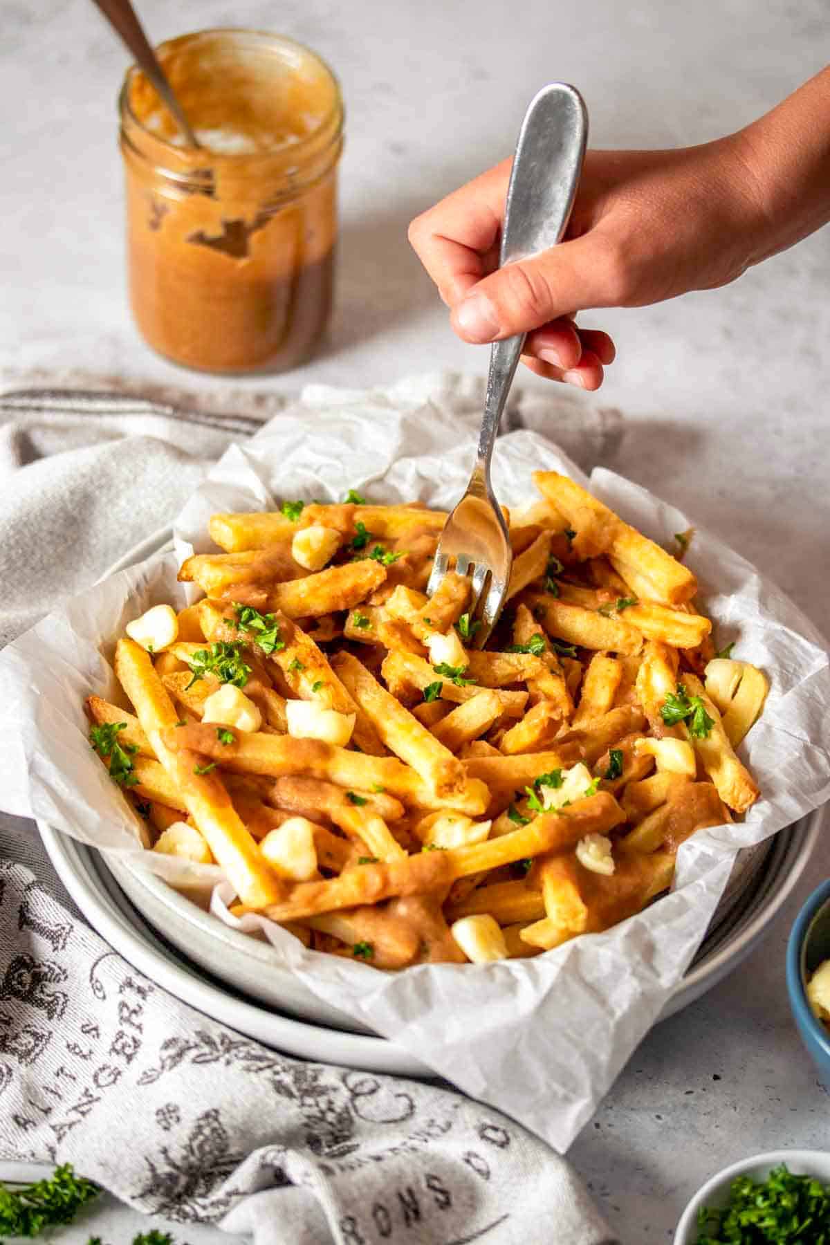 A hand with a fork getting a bite of vegan poutine from two stacked white bowls.