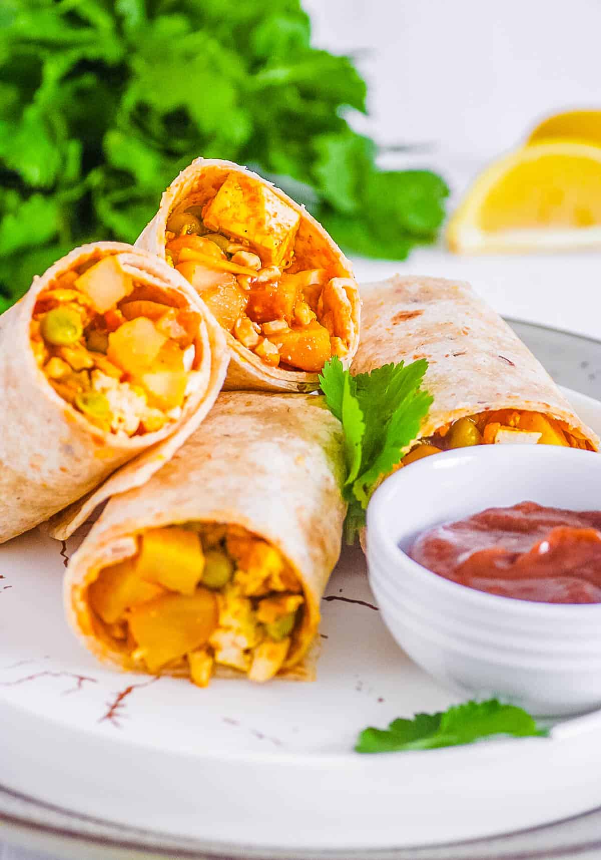 Indian samosa wraps cut in half and served on a white plate with chutney on the side.