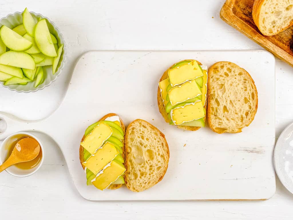 Apple and brie slices added to sourdough bread on a cutting board.