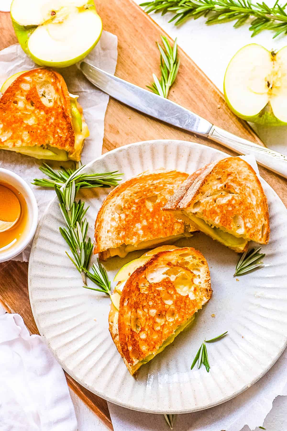 Sourdough grilled cheese sandwich with apple and brie cut and stacked on a plate with fresh herbs.