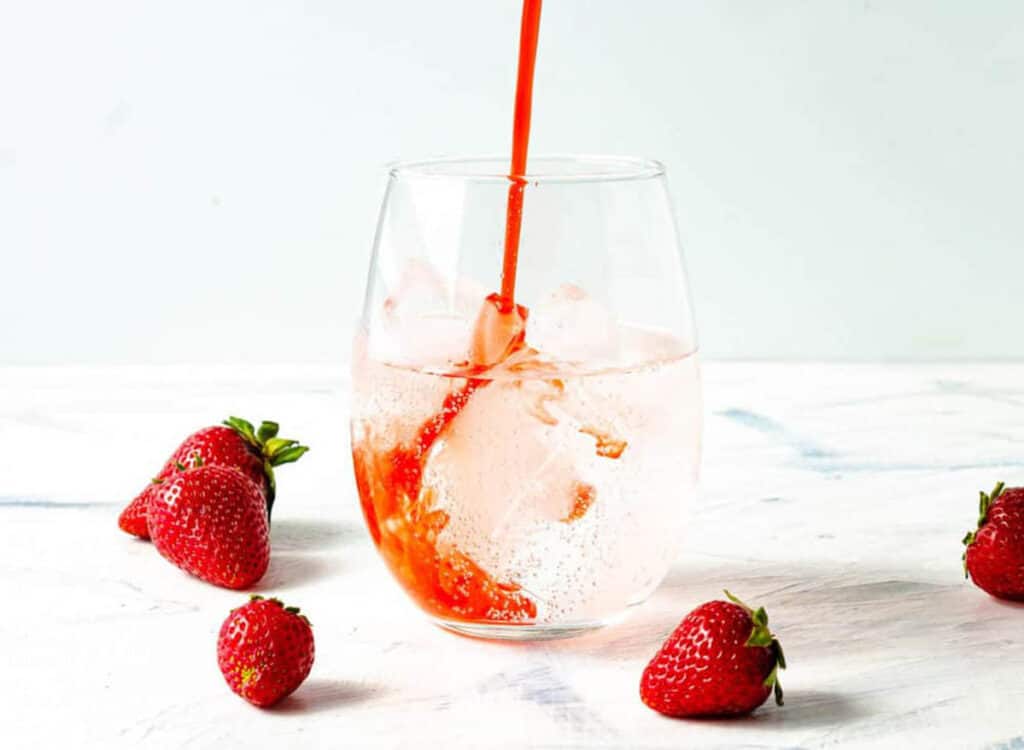Strawberry syrup poured into a glass with sparkling water.