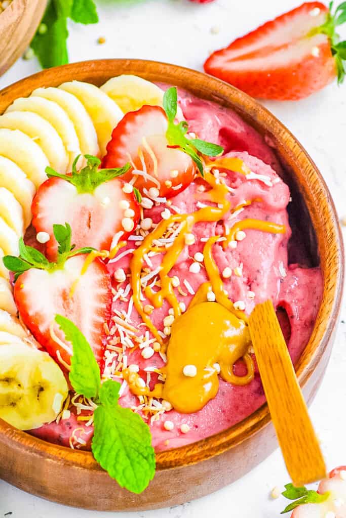 Closeup overhead shot of a Strawberry smoothie bowl topped with banana slices, strawberries, nut butters and seeds on a white countertop.