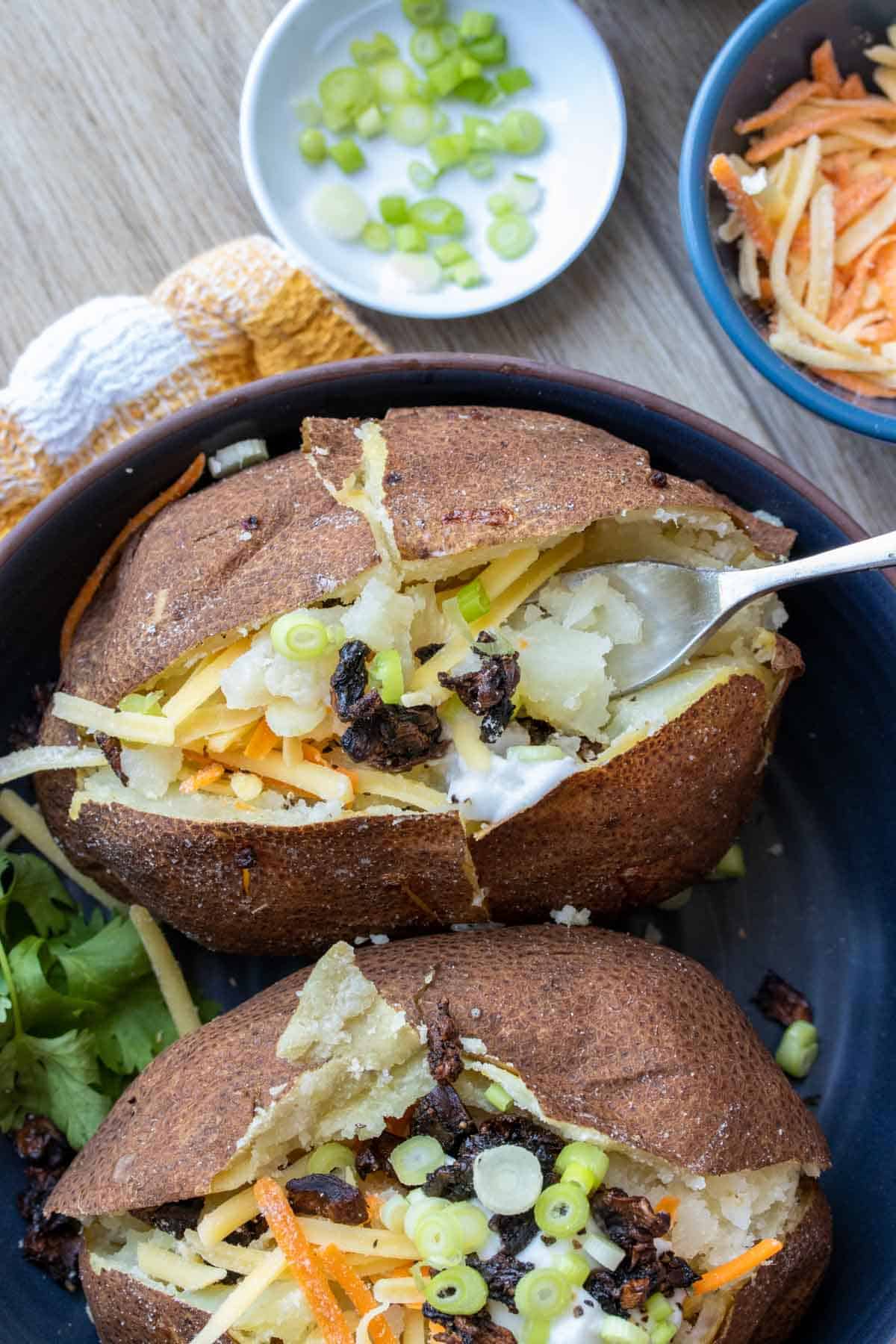 Fork getting a bite of a loaded baked potato that is in a blue bowl