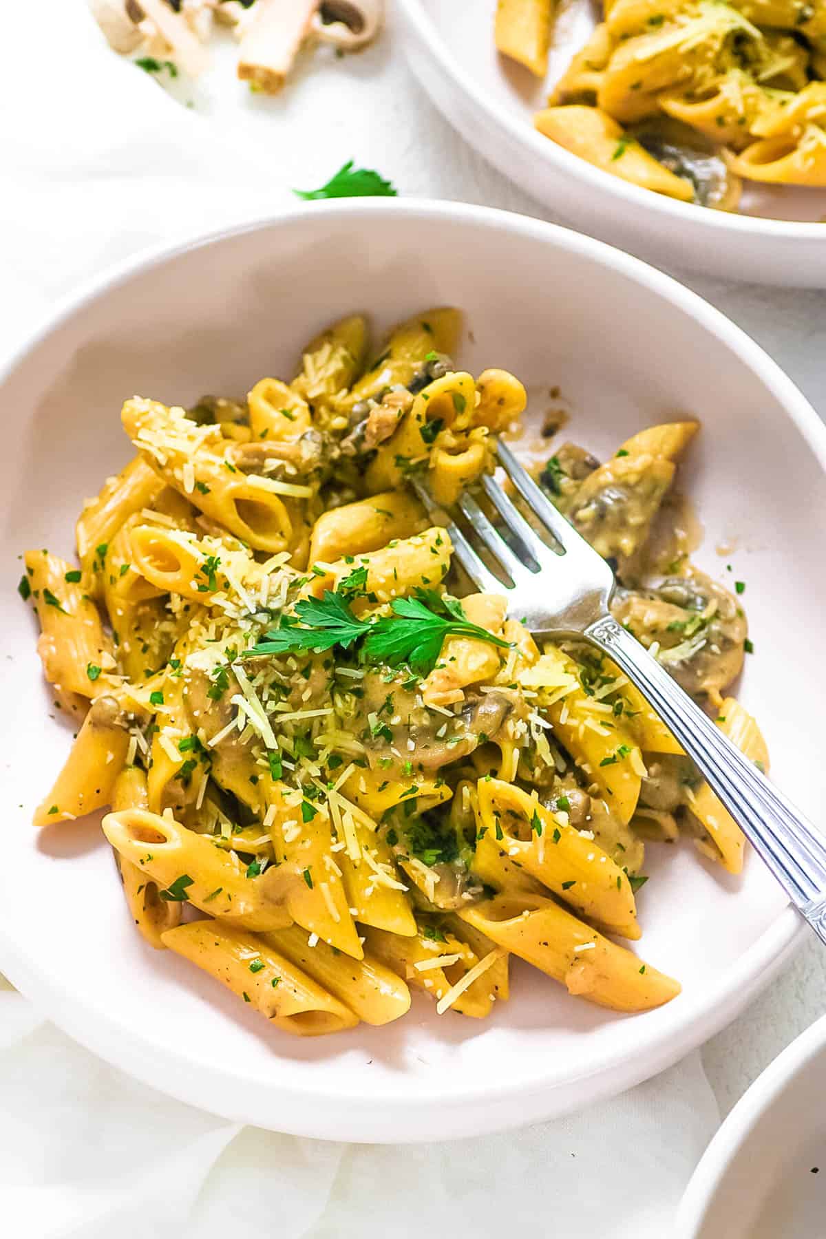 Vegan creamy mushroom pasta in a white bowl with a fork, topped with fresh herbs.
