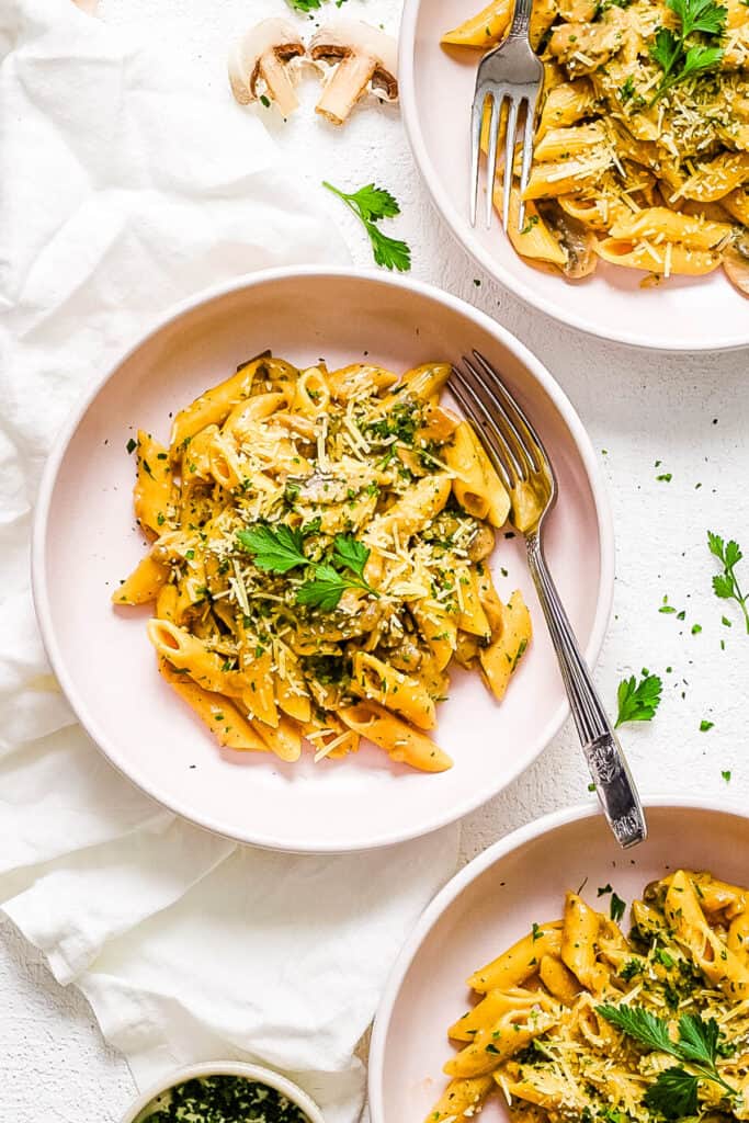 Creamy vegan mushroom pasta in a white bowl with a fork, topped with fresh herbs.