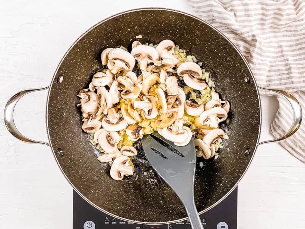 Mushrooms sauteeing in a skillet on the stove.