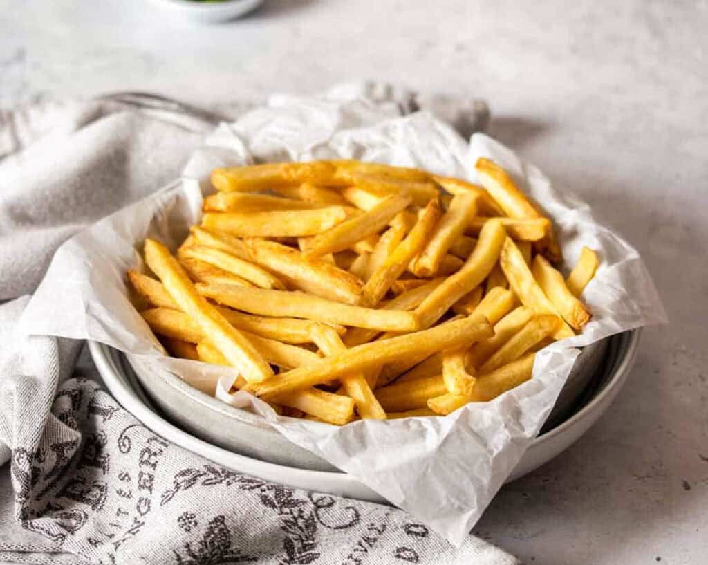 Two white bowls stacked on top of each other with parchment paper and french fries in them.