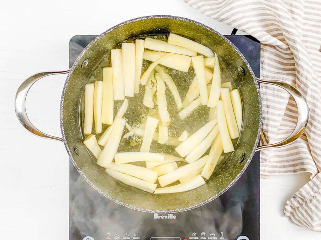 Yuca sticks boiling in a pot on the stove.