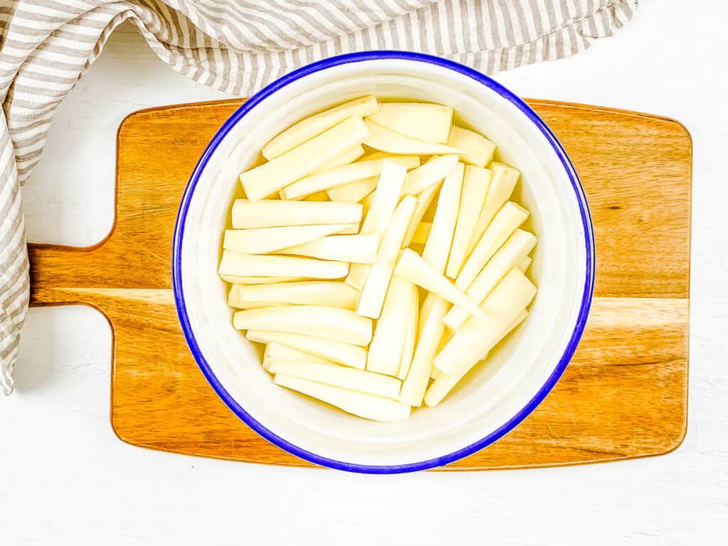 Cut yuca sticks soaking in a mixing bowl filled with water.