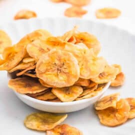 Air fryer banana chips in a white bowl, overflowing onto a white plate.