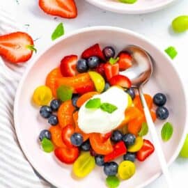 Low calorie breakfast fruit salad served in a white bowl, topped with yogurt and mint.