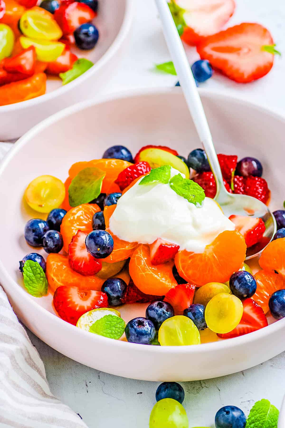 Easy breakfast fruit salad served in a white bowl, topped with yogurt and mint.