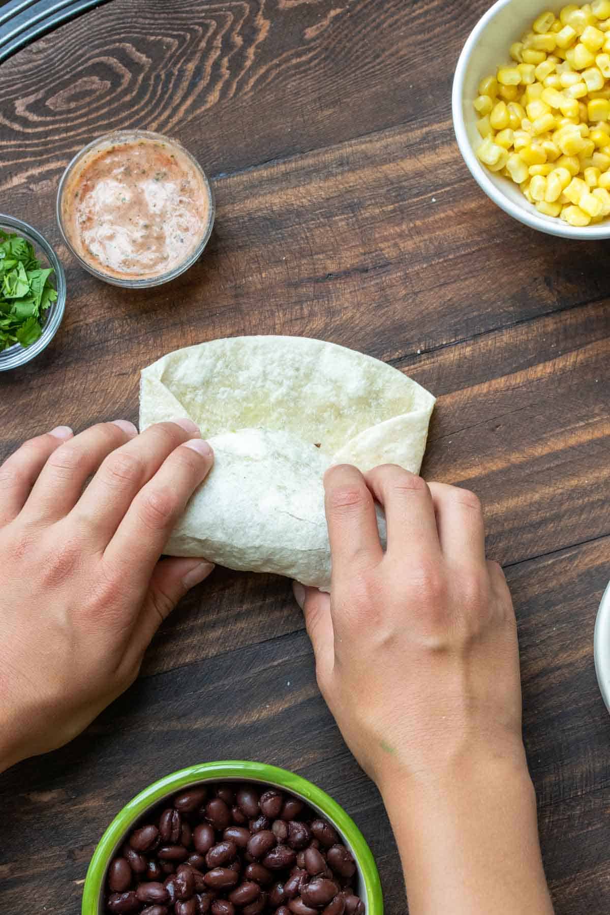 Hands rolling up a tortilla into a burrito on a wooden table