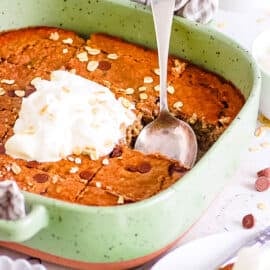 Vegan high protein baked oats in a green baking dish, topped with whipped cream.