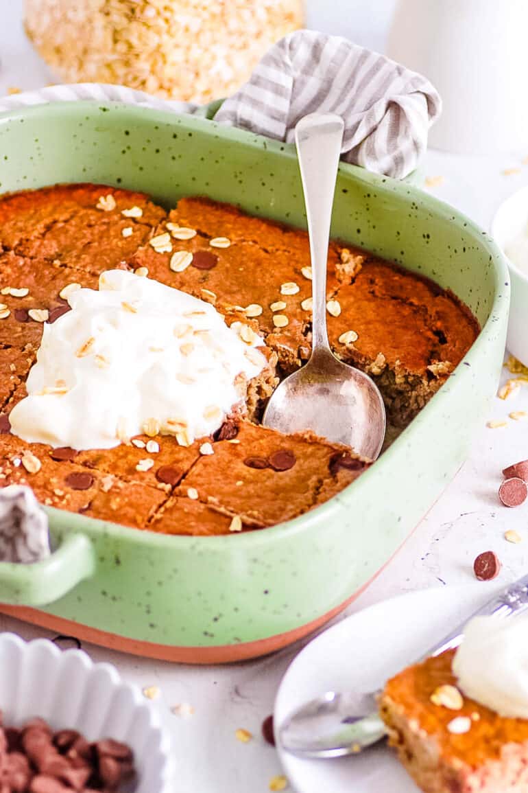 Vegan high protein baked oats in a green baking dish, topped with whipped cream.
