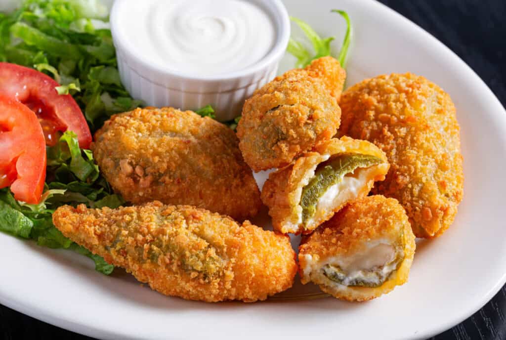 Close-up of jalapeno poppers with sour cream on a white plate.