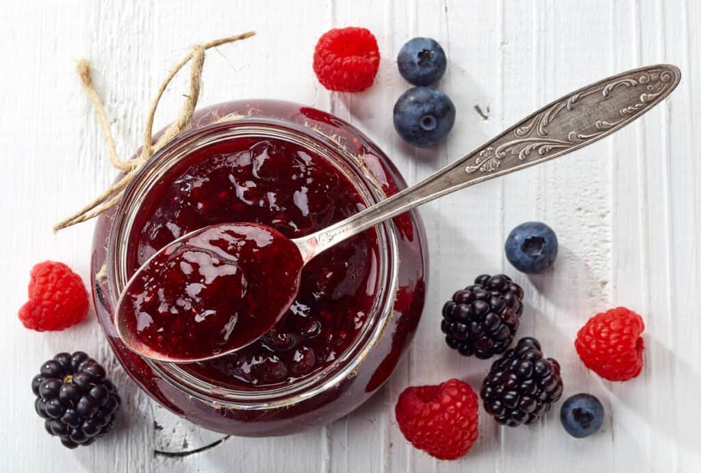 Jar of wild berry jam on white wooden background from top view.