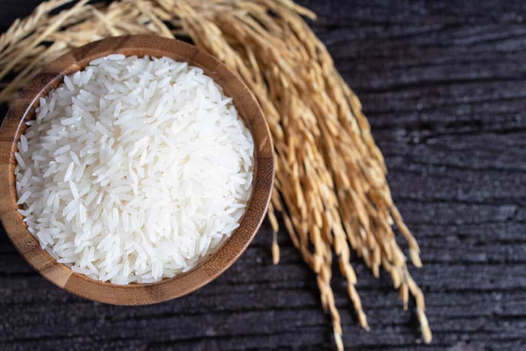 Top view of White rice (Thai Jasmine rice) in wooden bowl and paddy rice on dark wooden texture background.
