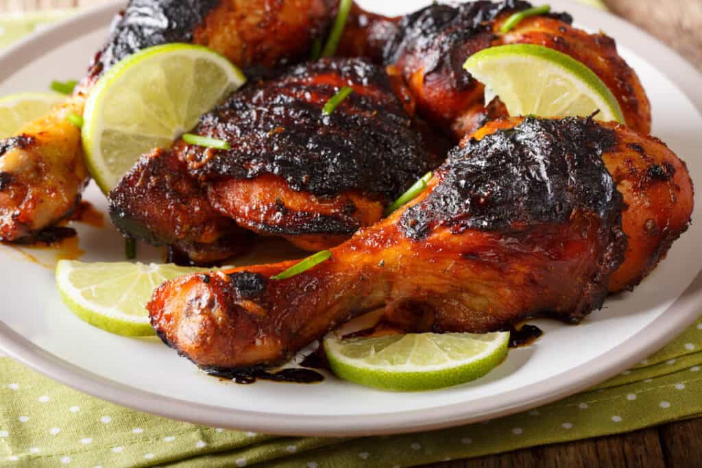 Jamaican food: jerk chicken drumstick with lime closeup on a plate on the table.