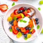 Low calorie breakfast fruit salad served in a white bowl, topped with yogurt and mint.
