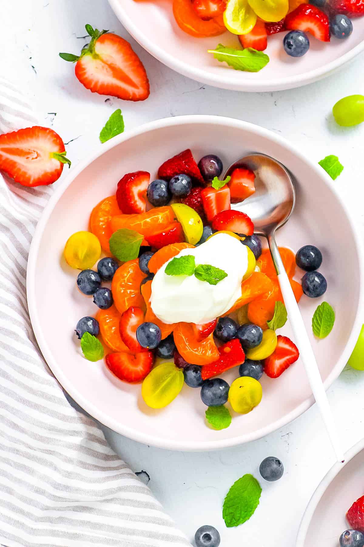 Low calorie breakfast fruit salad served in a white bowl, topped with yogurt and mint.