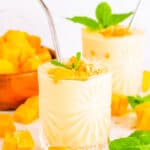 Healthy mango protein smoothie served in a gl،, garnished with mango c،ks and mint.