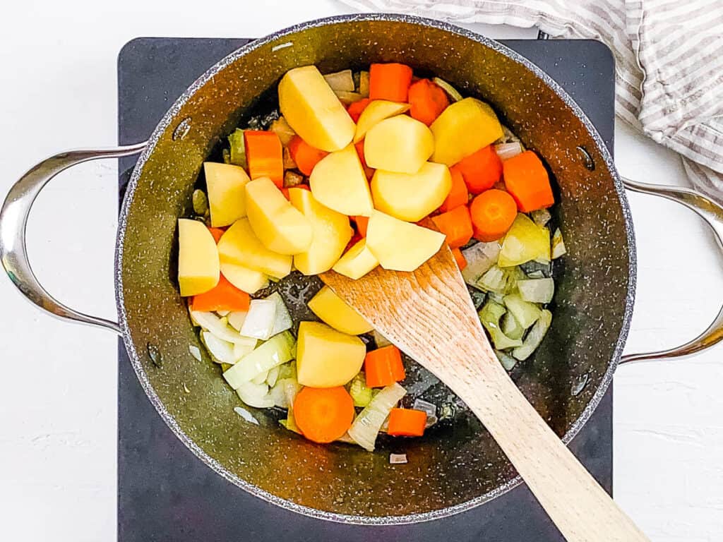 Onions, carrots and potatoes sauteed in a pot on the stove.