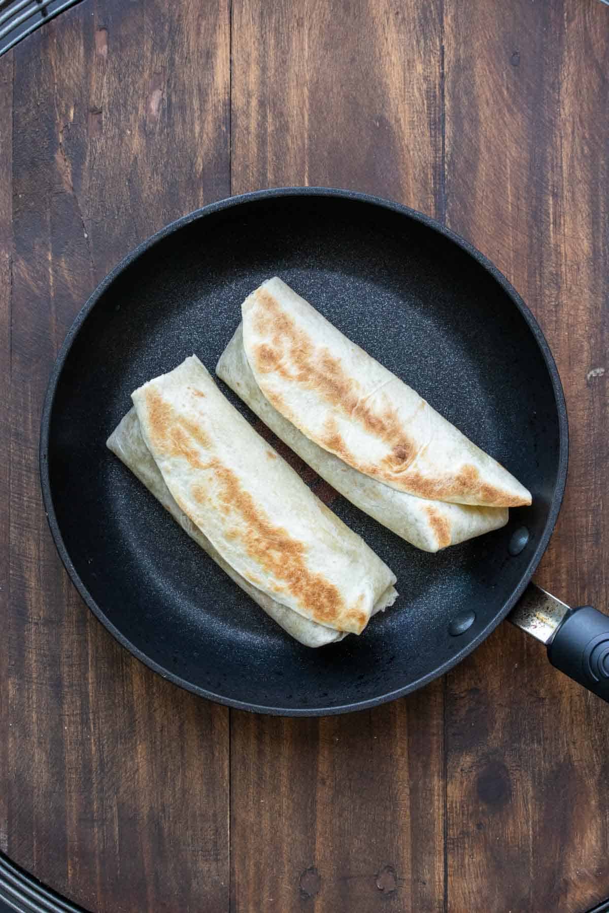 Pan with two burritos grilling on it