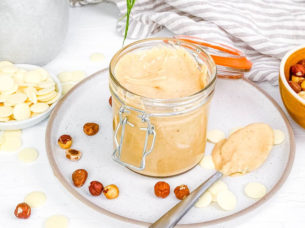 White chocolate nutella stored in a mason jar, place on a plate with a spoon.