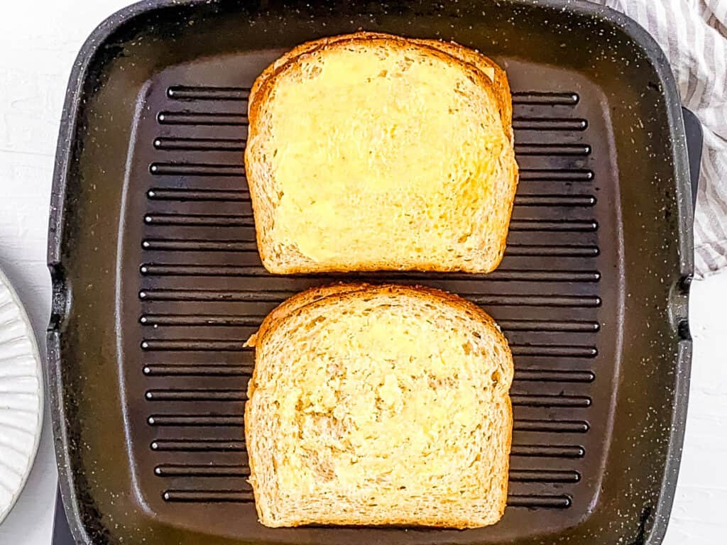 Grilled cheese and pickles cooking on a grill pan.