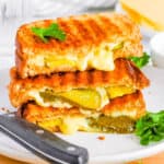 Grilled cheese with pickles, sliced and stacked on a white plate.