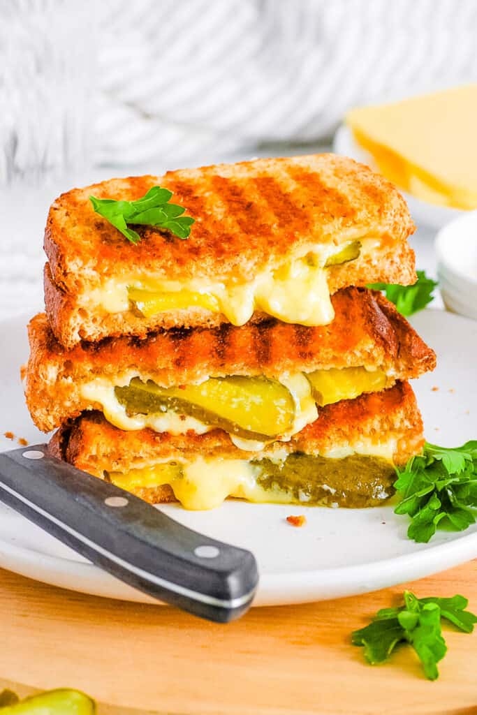 Grilled cheese with pickles, sliced and stacked on a white plate.