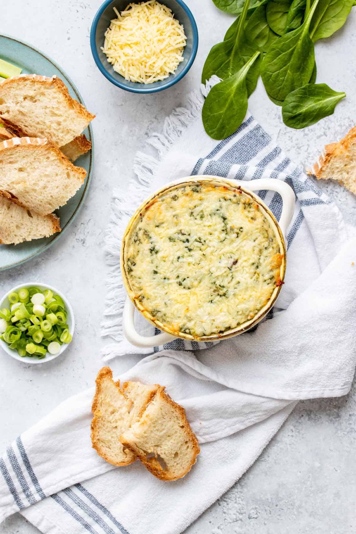 Top view of a white soup bowl with a baked spinach dip crusted with parmesan cheese on top sitting on a white towel with blue stripes