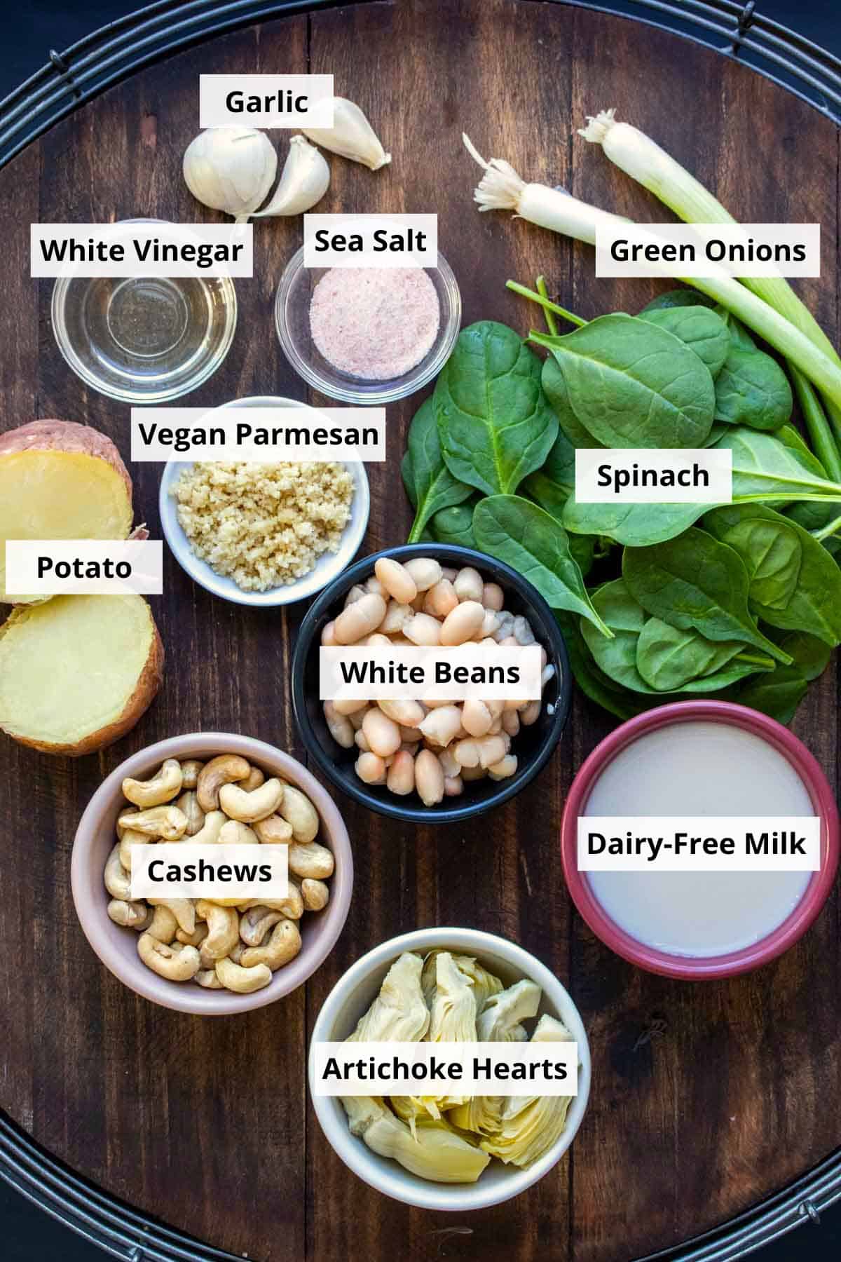 Ingredients for making a dairy free spinach artichoke dip in bowls and on a wooden surface