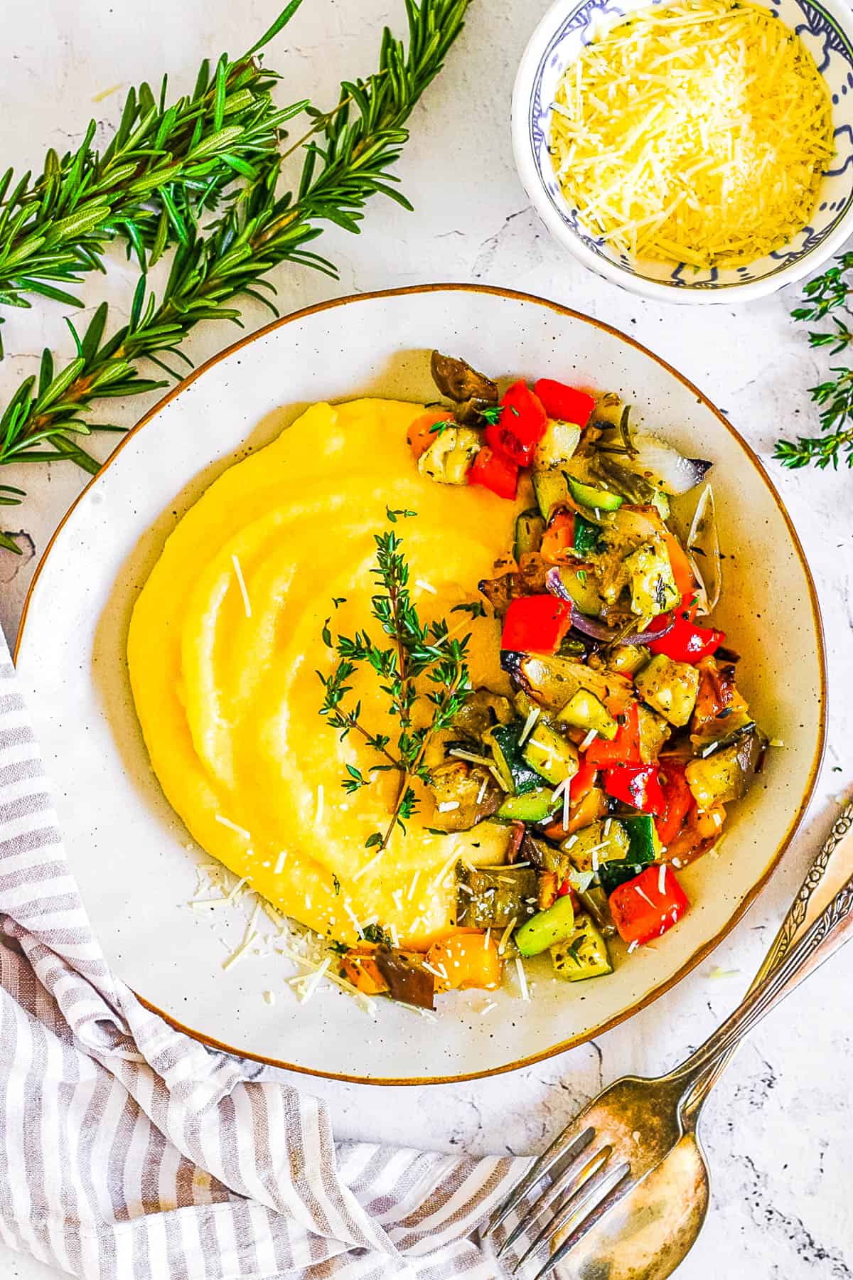 Vegetable polenta with parmesan served in a white bowl garnished with fresh herbs.