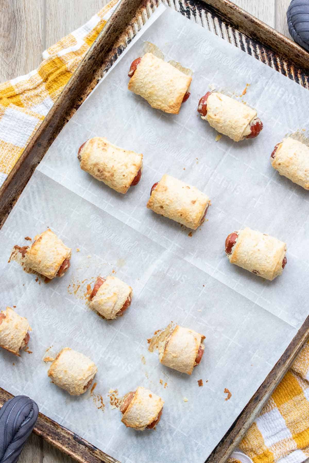 Baked vegan pigs in a blanket on a parchment lined baking sheet.