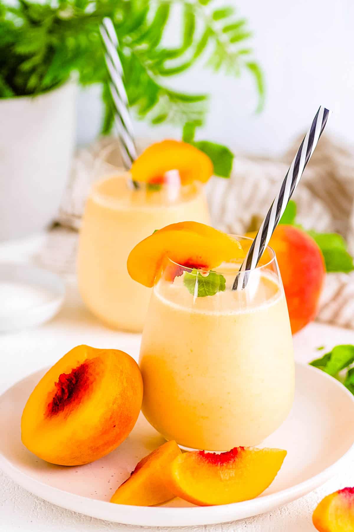 Peach milk drink served in a glass with a straw and garnished with fresh peaches.