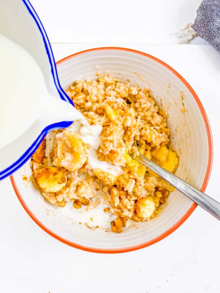 Milk added to banana cream oatmeal in a white bowl.