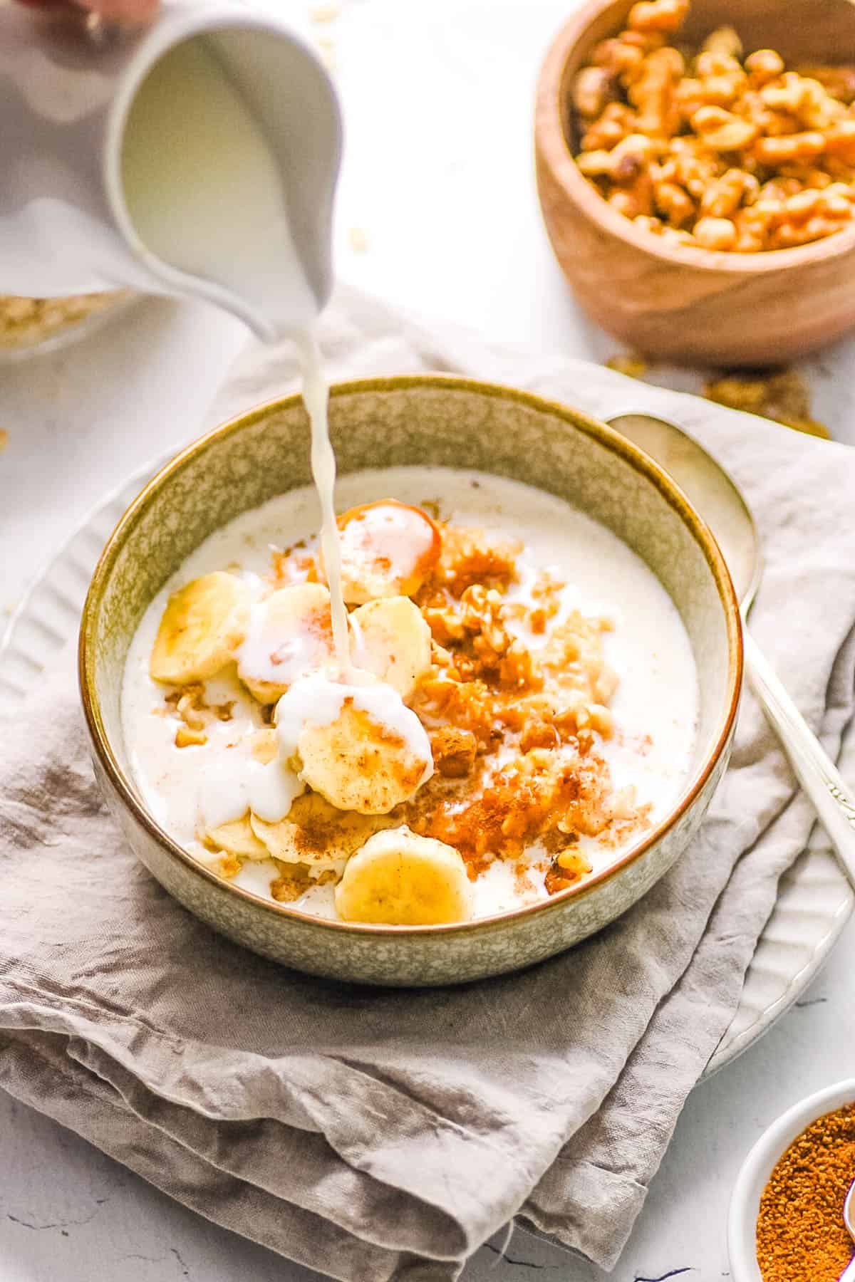 Healthy bananas and cream oatmeal in a bowl, topped with milk.