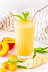 Peach banana smoothie served in a glass with a straw and mint leaves as a garnish.