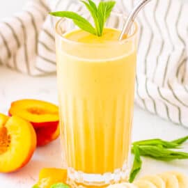 Peach banana smoothie served in a glass with a straw and mint leaves as a garnish.