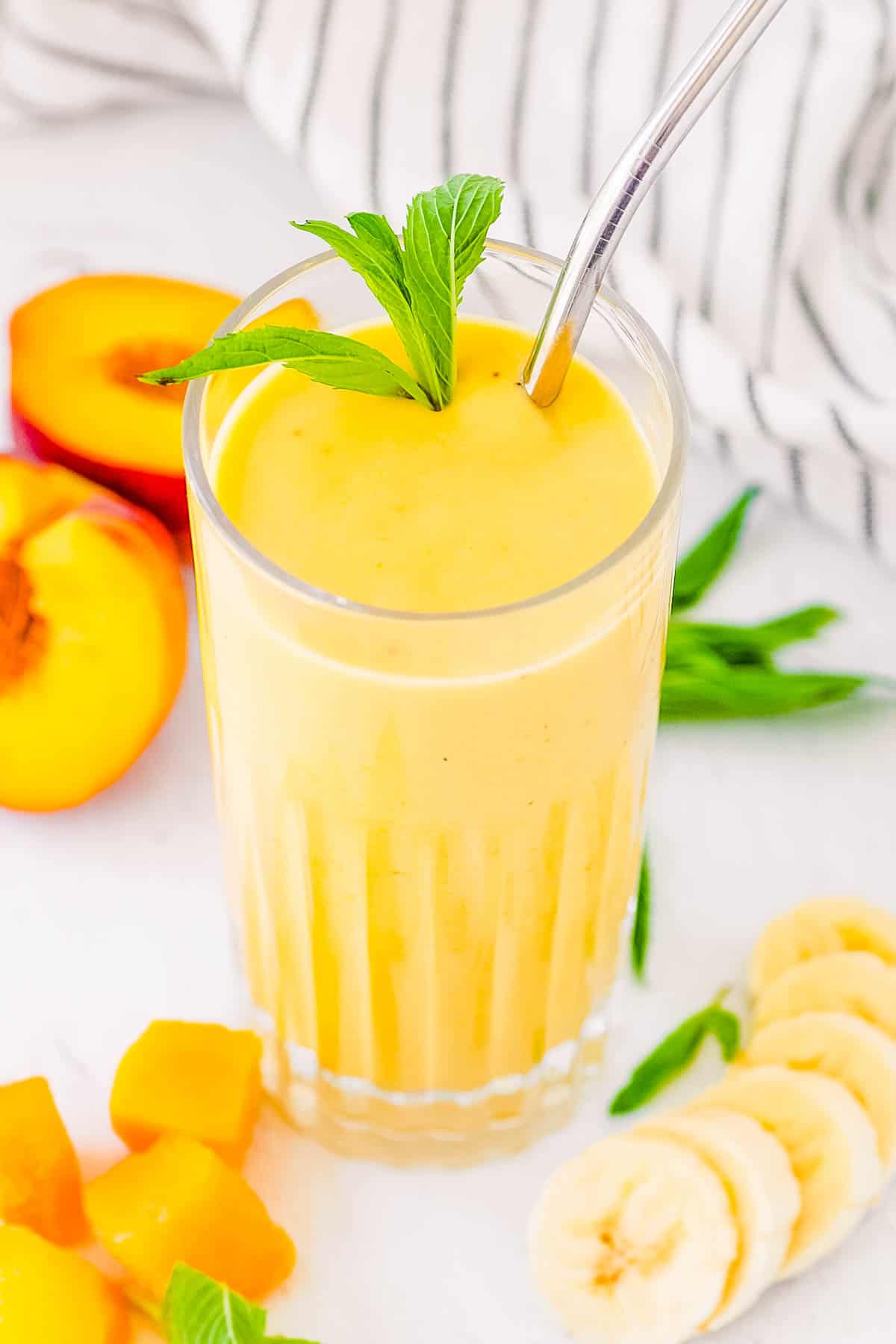 Banana peach smoothie served in a glass with a straw and mint leaves as a garnish.