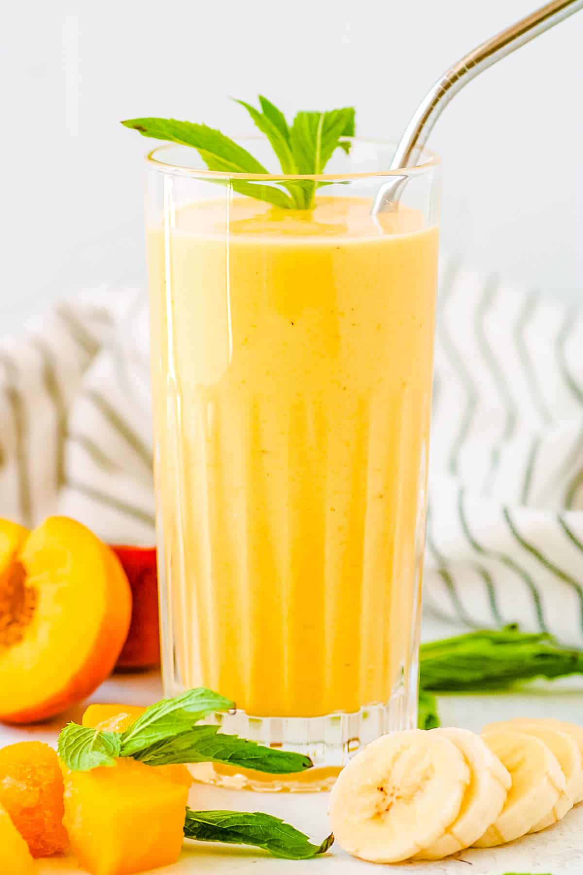Banana peach smoothie served in a glass with a straw and mint leaves as a garnish.