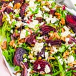 Roasted beet and feta salad with walnuts and mixed greens, served on a large white serving platter.