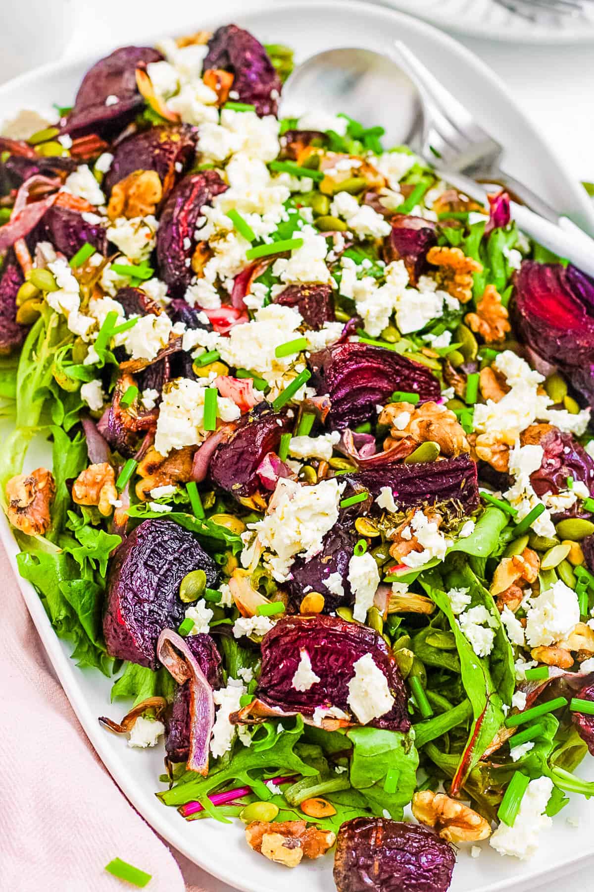 Roasted beet and feta salad with walnuts and mixed greens, served on a large white serving platter.