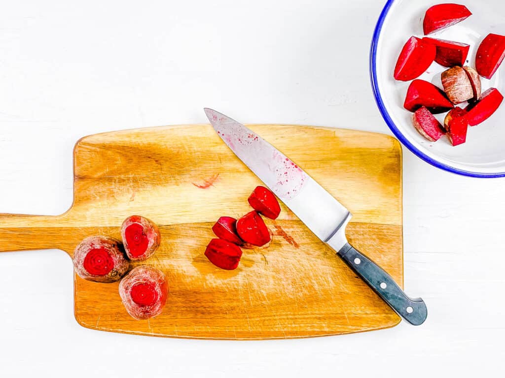 Baby beets cut into halves on a cutting board.