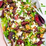 Roasted beetroot and feta salad with walnuts and mixed greens, served on a large white serving platter.